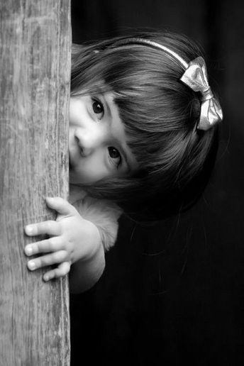 une petite fille qui se cache à moitié derrière une porte