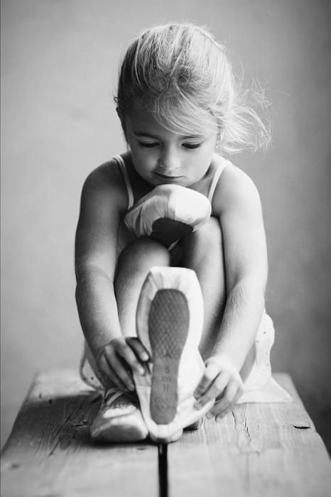 Une petite fille qui mets ses chaussons de danse , photo noir et blanc .