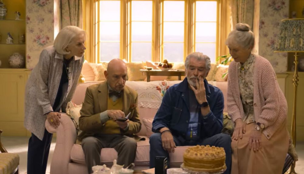 A still from the Thursday Murder Club movie showing the 4 leads sitting on  couch together in front of a cake. 