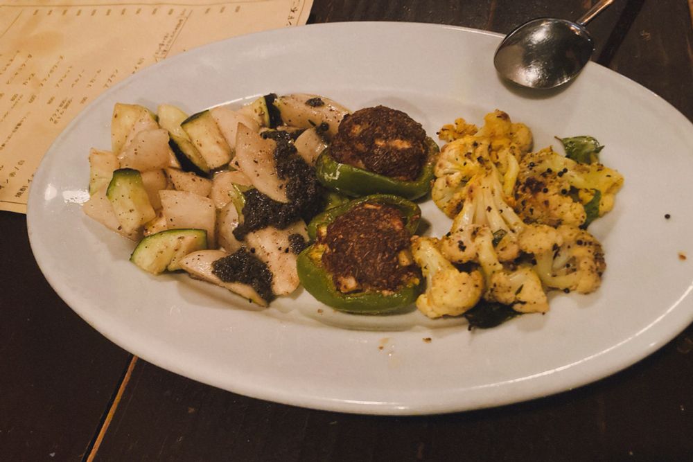 白い楕円の皿に料理がのっている写真。
右上にスプーンが置かれている。
右端にはカリフラワー、中央に半分に割ったピーマンに茶色いものが詰まったもの、左に白い野菜が一口大に乱切りされたものと並んでいる。さ