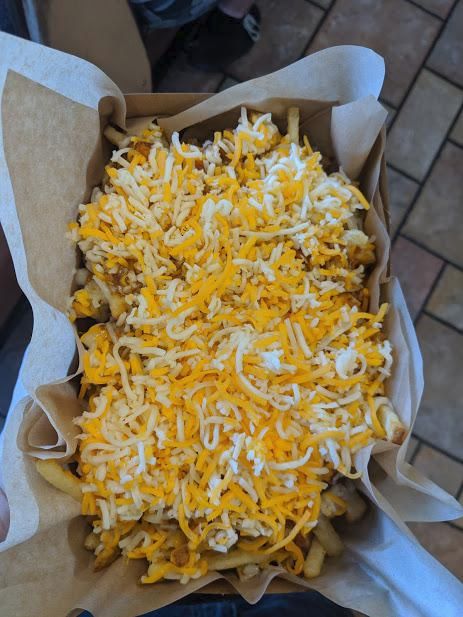 A large cardboard basket of shredded cheese under which a few fries and some chili are peeking out.