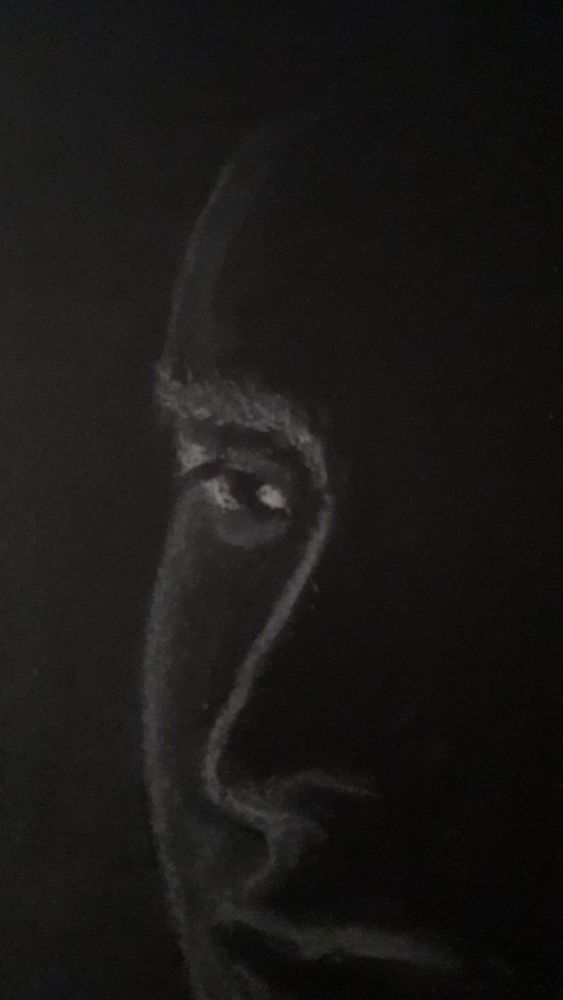 Closer up version of the other photo, which was a drawing of a silhouette side profile of someone's face, with white charcoal on black paper. Person is in deep thought, looking across