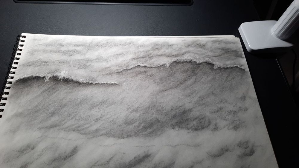 Photo of my charcoal sketch on a pad, of stormy, moving waves, with the base of my lamp in the top, right corner