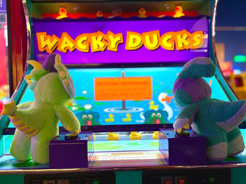 Photo of arcade game "Wacky Ducks" with Rawrcade plushies Cade and Fizz sitting on top of and playing. 