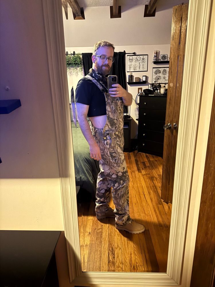 Mirror selfie of me in a black crop top with camouflage overalls, and tan boots. 