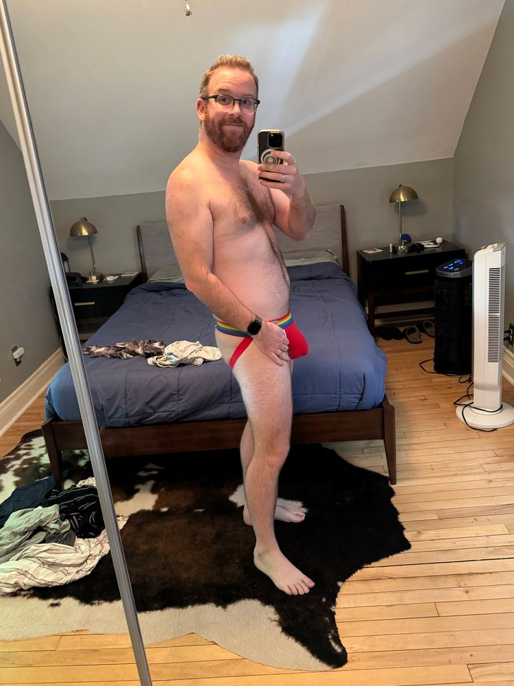 A mirror photo of the same man without the shirt this time. He is standing facing sideways so his bulge is more visible and his cheeks are showing. 
