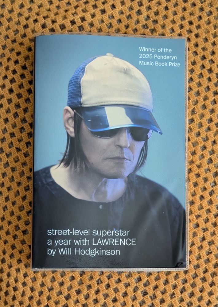 Street-level superstar: a year with LAWRENCE by Will Hodgkinson, paperback on orange blanket 
