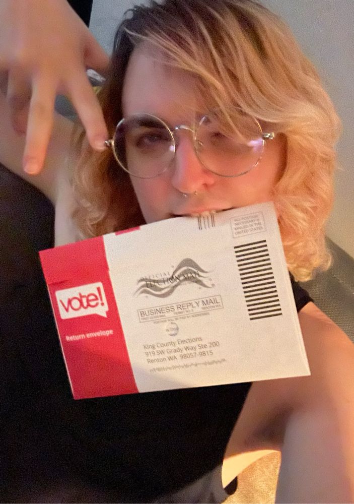 Selfie containing a sealed election ballot, subject is holding onto the envelope by biting the corner.
