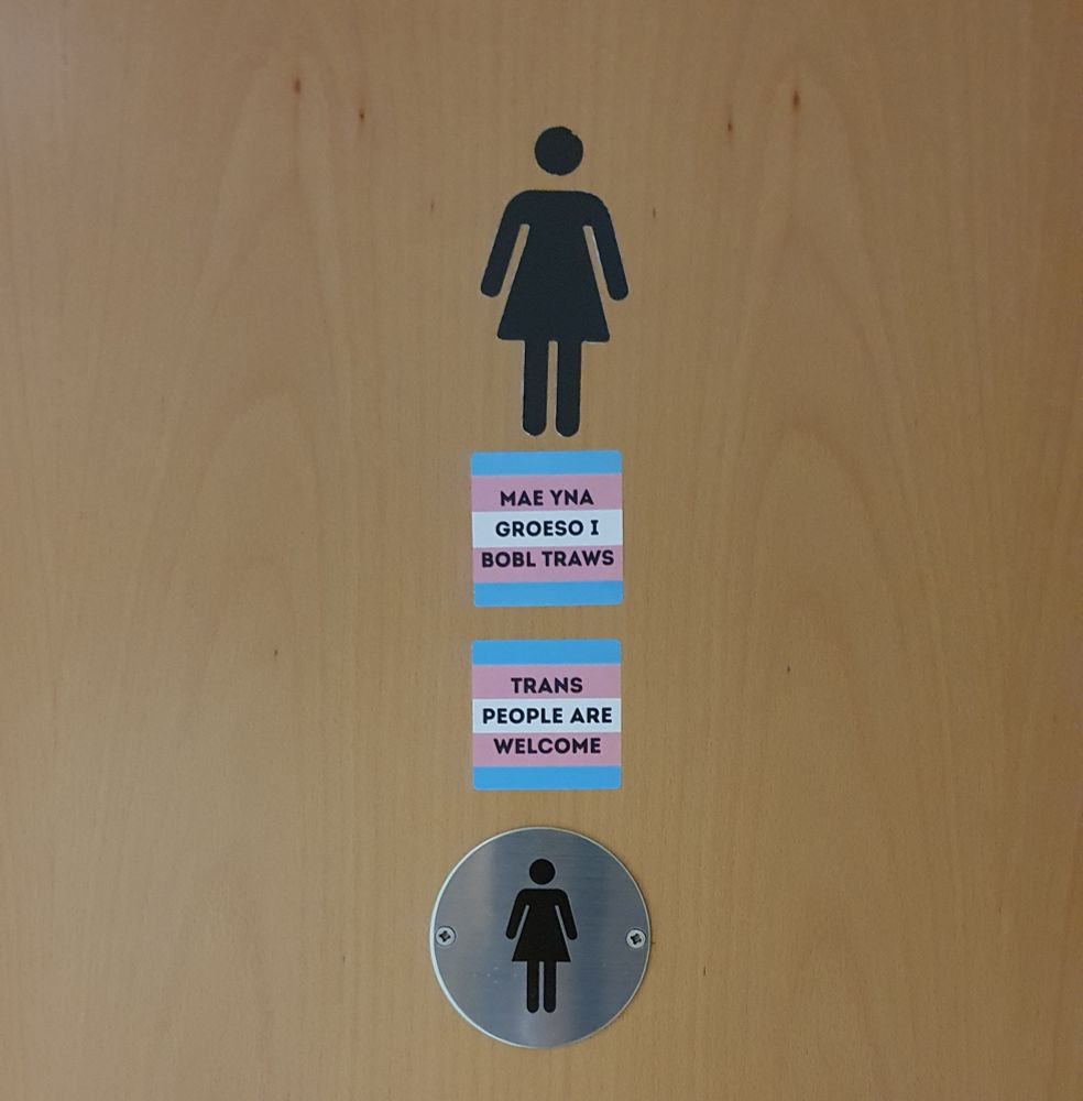 Fully bilingual stickers indicating that the toilets pictured are trans-inclusive.