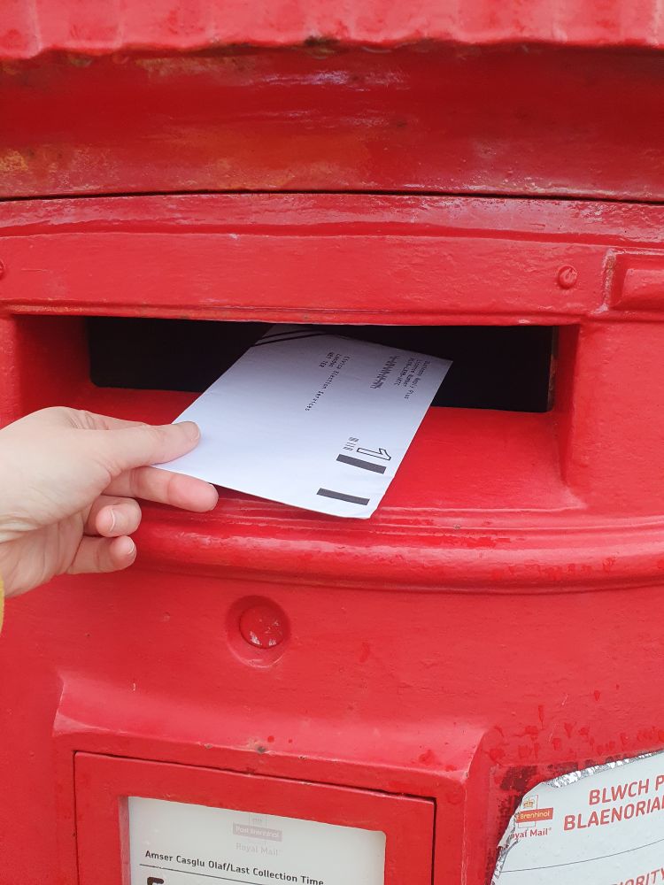 An envelope containing a UCU ballot paper being posted in a red post box.