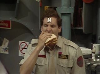 Arnold Rimmer, a character in the BBC sitcom Red Dwarf, eats a sandwich. His expression suggests he is not sure about it.