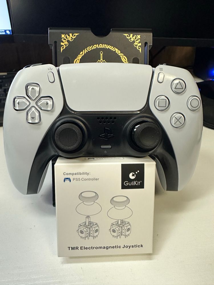 White Dualsense Controller for PS5 with GuliKit TMR analog sticks installed. Below the controller is the box for the GuliKit TMR analog sticks.