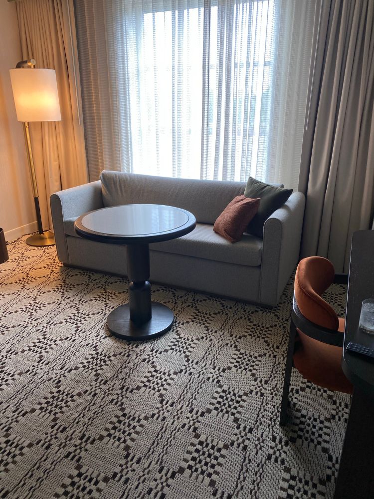 A gray couch, a round table, and an orange desk chair in a hotel room 
