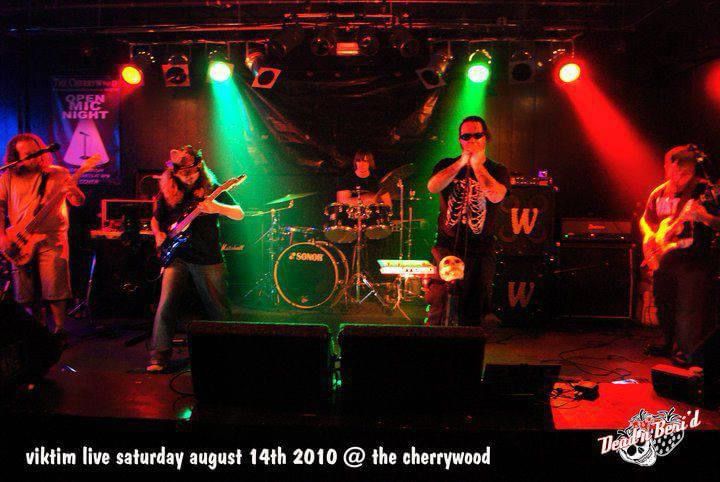 New jersey cyberpunk band viktim performing in blackwood NJ at a bar called The cherrywood. Stage is all red with green highlights.  There is a full band on stageL-R: Chris Novelli (bass/synth), Jen Pallante (guitar, vox), Scotty (drums), Kristen Eddie Threat (vix/samples/grinder), Cannon (guitar/vox).  Venue was The Cherrywood, a bar that did metal nights, this was the last night before they sold the liquor license and permanently closed. 
