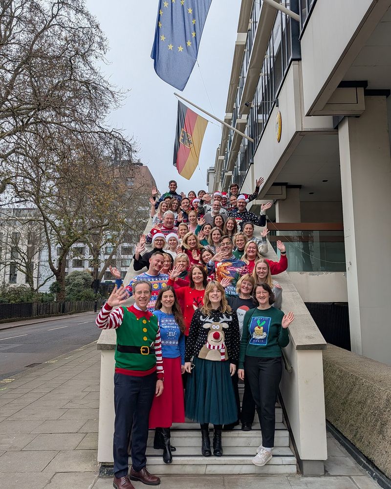 People stood on the steps of the German Embassy wearing Christmas jumpers and waving 
