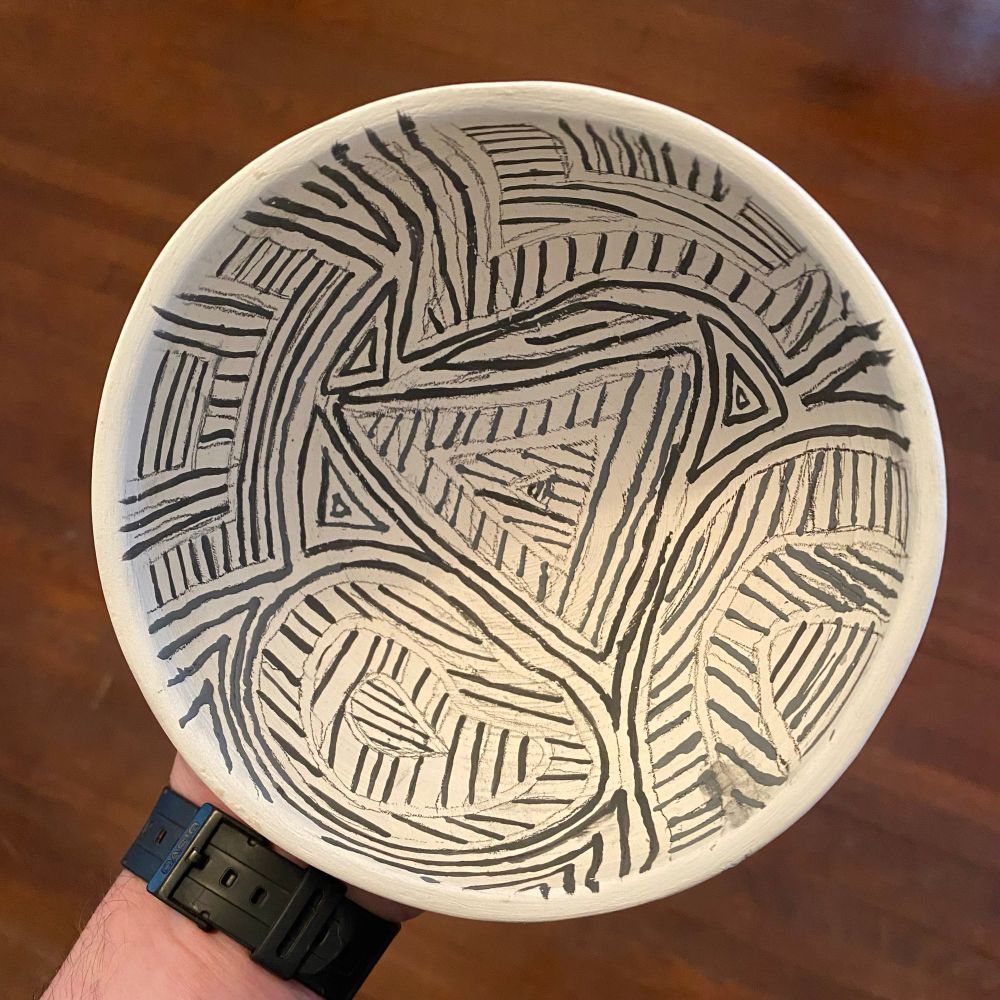 A picture of the inside of a handmade white ceramic bowl is painted with various black lines 