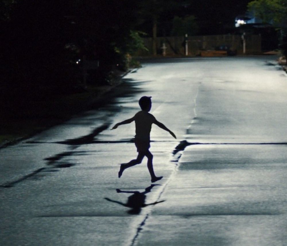 grainy night shot from the movie Weapons of a kid in sprinting across a deserted street late at night 
