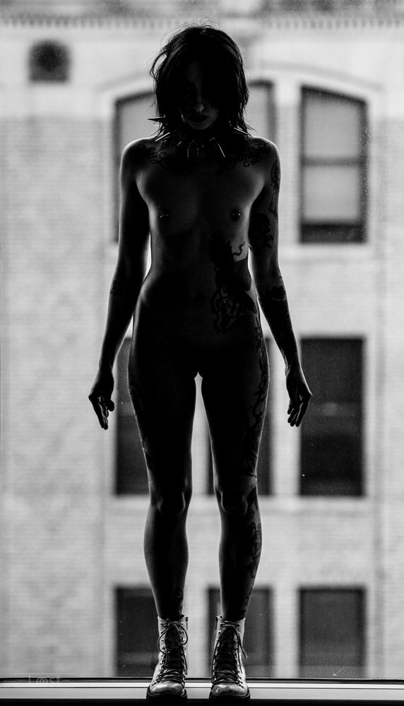 Black and white photo of a nude woman in silhouette with the wall of a building seen behind her