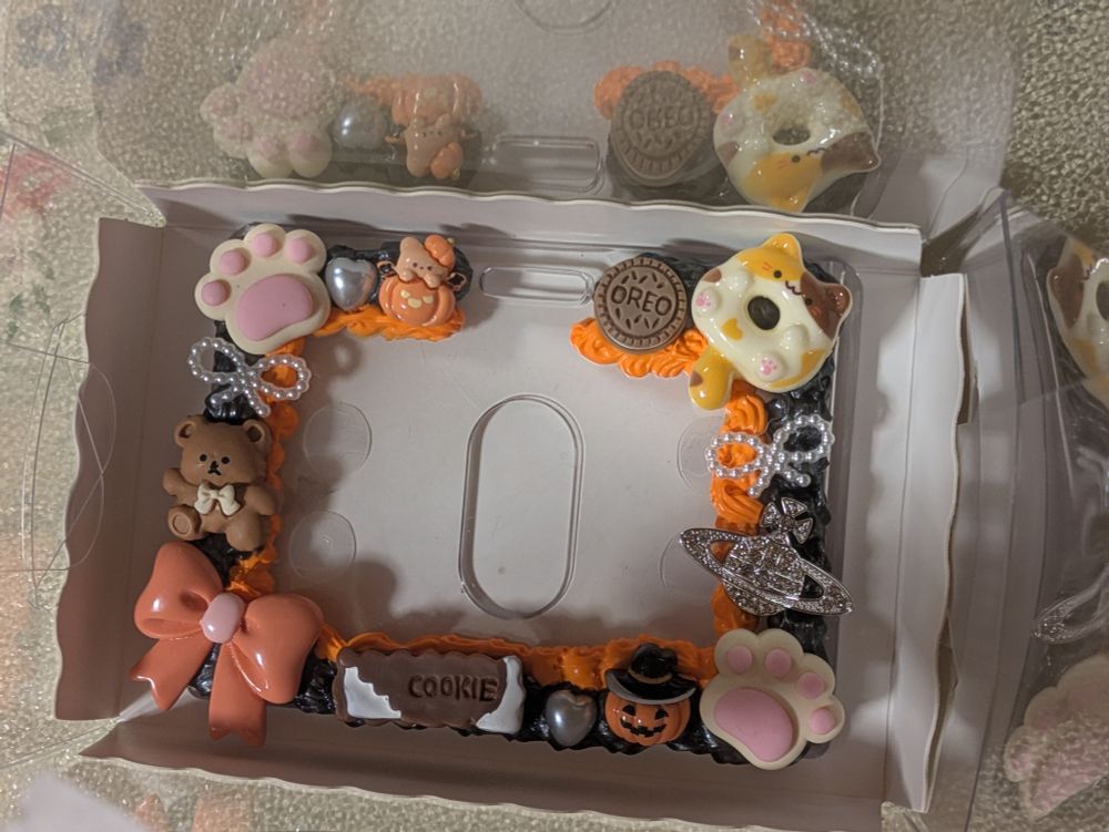 A black x orange ID badge holder with cat, sweets, bows, and Halloween themed charms deco'd onto it