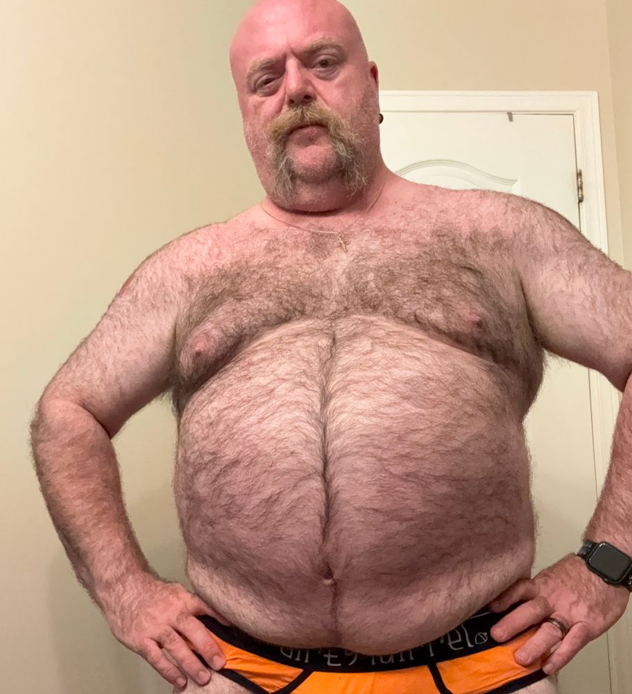 Hairy man wearing orange briefs with no shirt. 