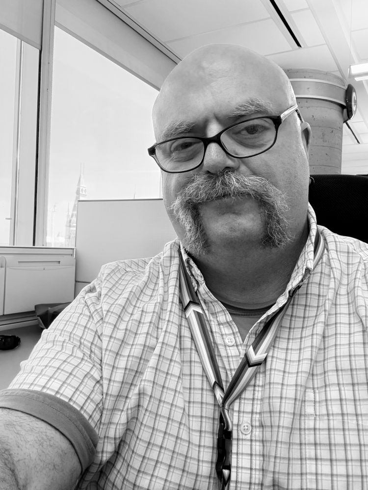 Black and white photo of man with handlebar moustache in an office setting. 