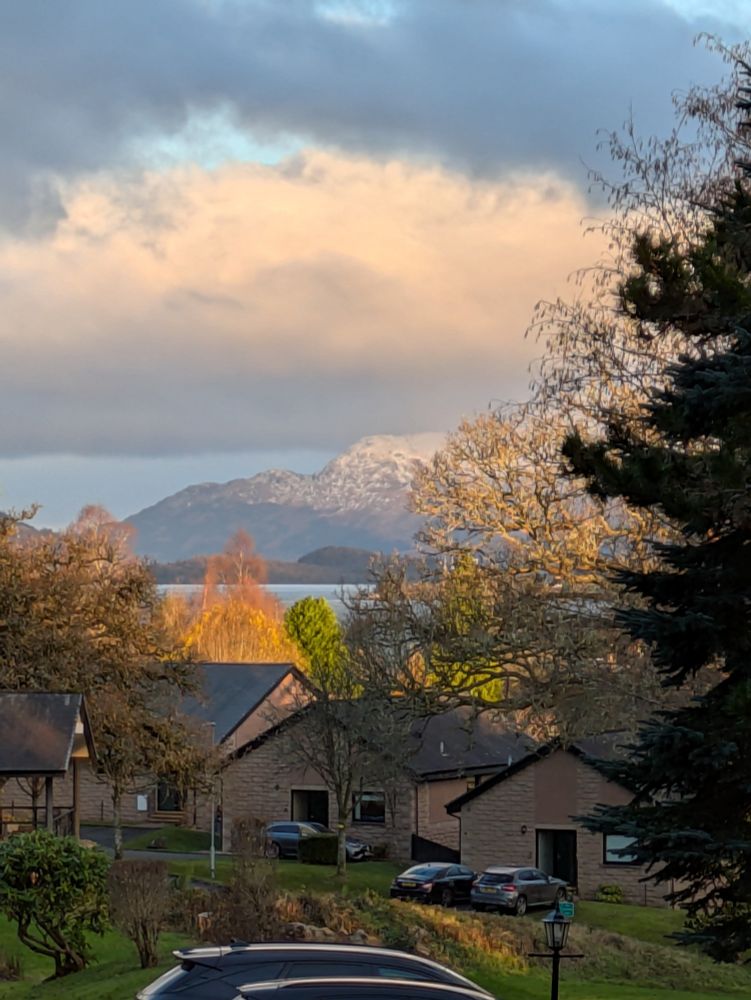 Photo of mountains cloaked in frosty mist, across Loch Lomond and some little cabins and cars closer to the photographer.