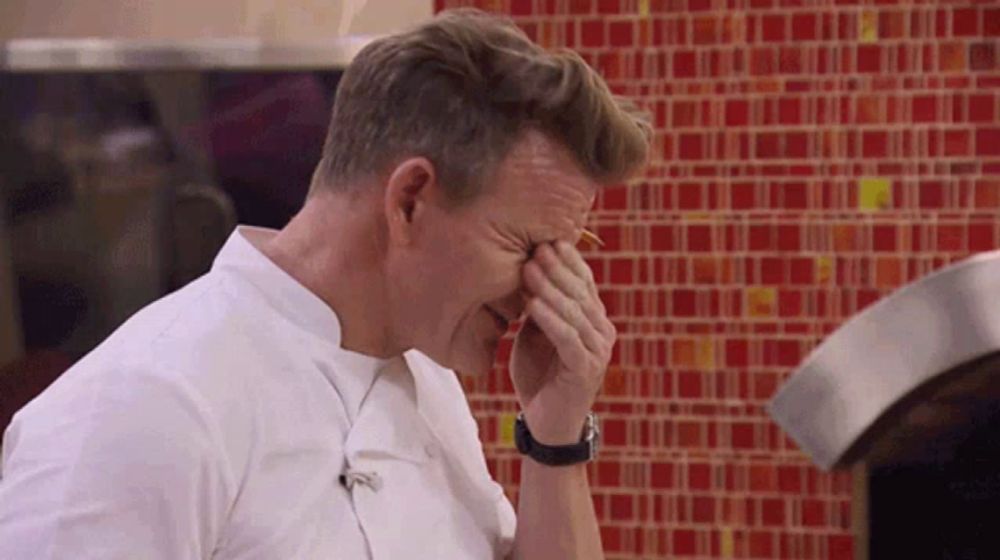 a man in a chef 's uniform wipes his nose with his hand