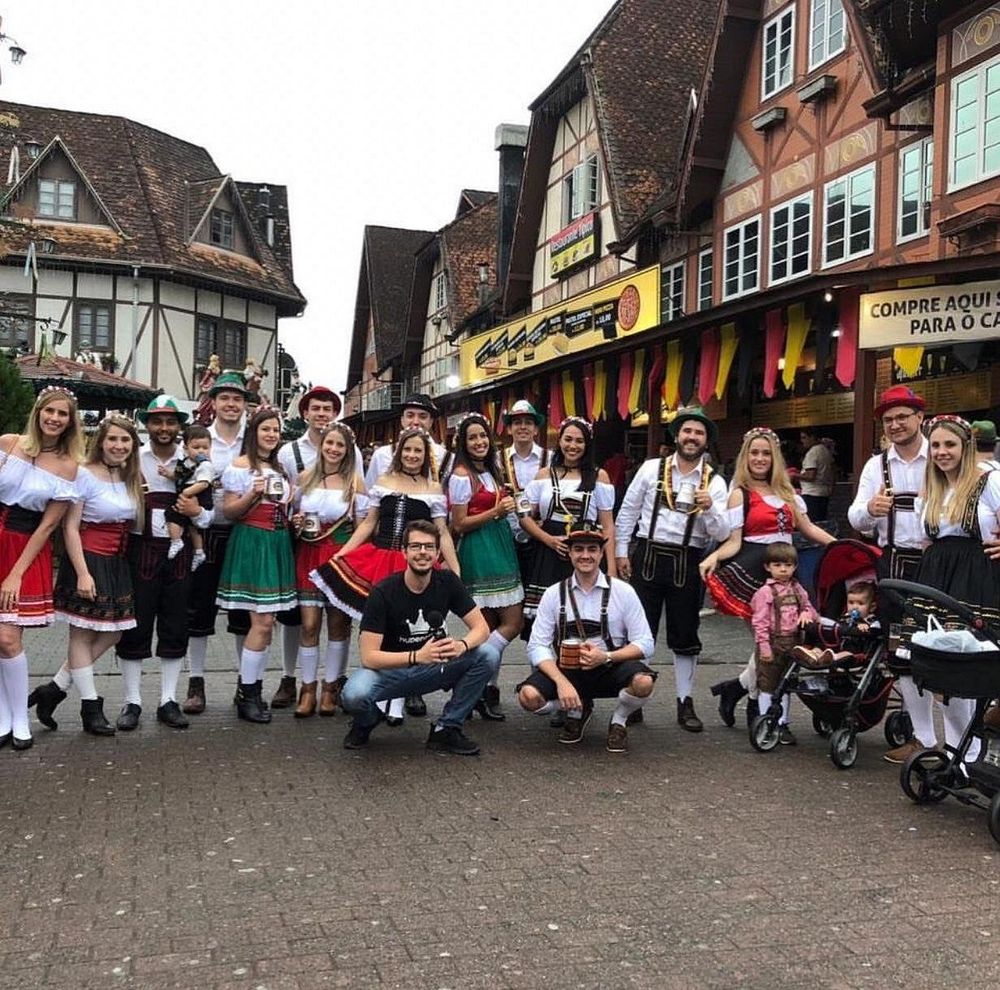 Bild von Blumenau mit Oktoberfestbesuchern. Männer in lederhosen, Frauen in Dirndln vor einer fachwerkhauskulisse.