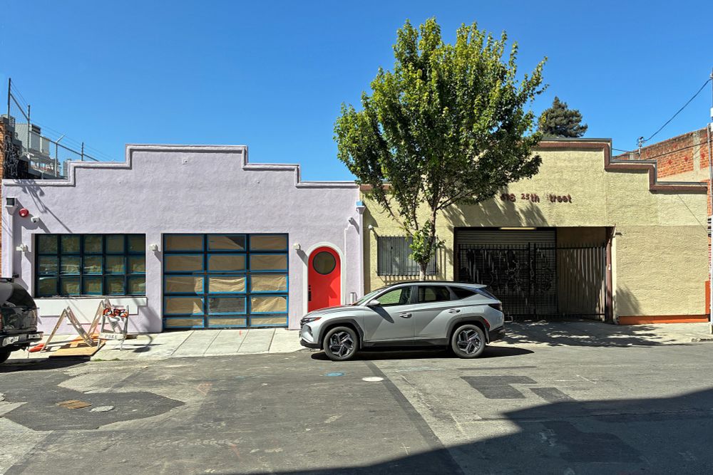 cute matching pair of step-fronted small warehouses; the one on the left has fresh lilac paint with trim being touched up and a bright red door with a semicircle doorway and round glass window.
