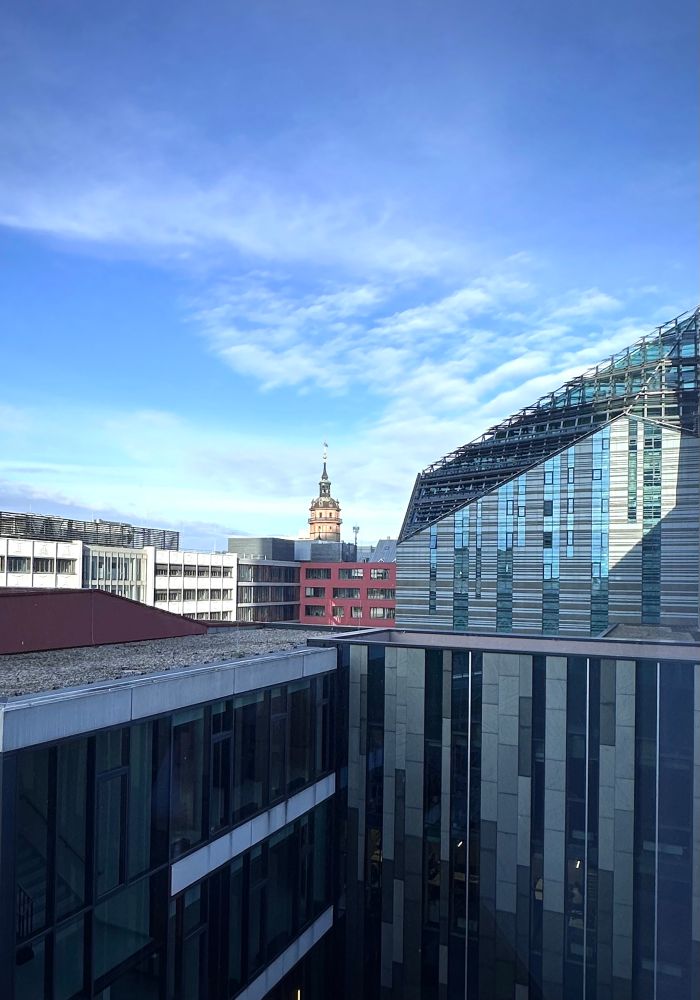 Blick über die Leipziger Innenstadt. Man sieht die gläsern Fassade des Paulinums der Universitären. Einige Dächer und im Hintergrund die Spitze der Nikolaikirche.