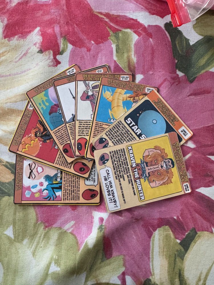 8 "Deadpool's Guide to Super Villians" trading cards fanned out on a table.  The top one is Kraven the Hunter.