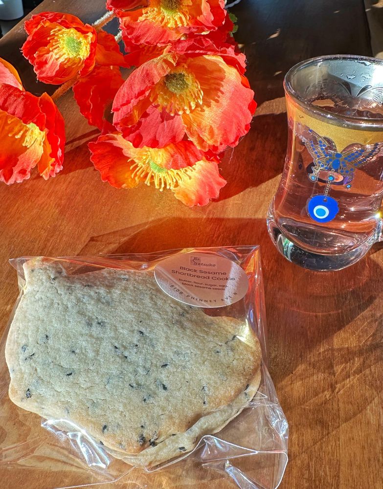 A sundrenched cafe counter with a bouquet of poppies, a teacup of pink tea, and a packet of cookies