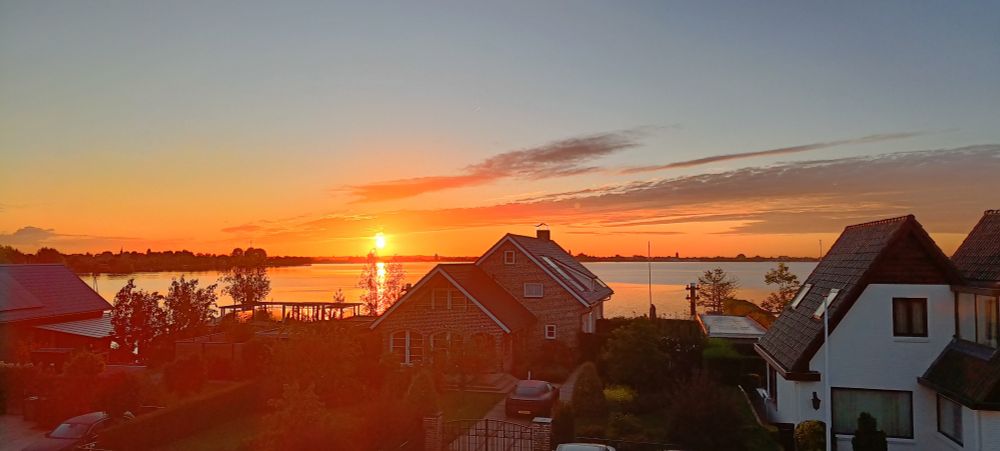 Sunrise over a lake. Houses part silhouetted in the foreground.
