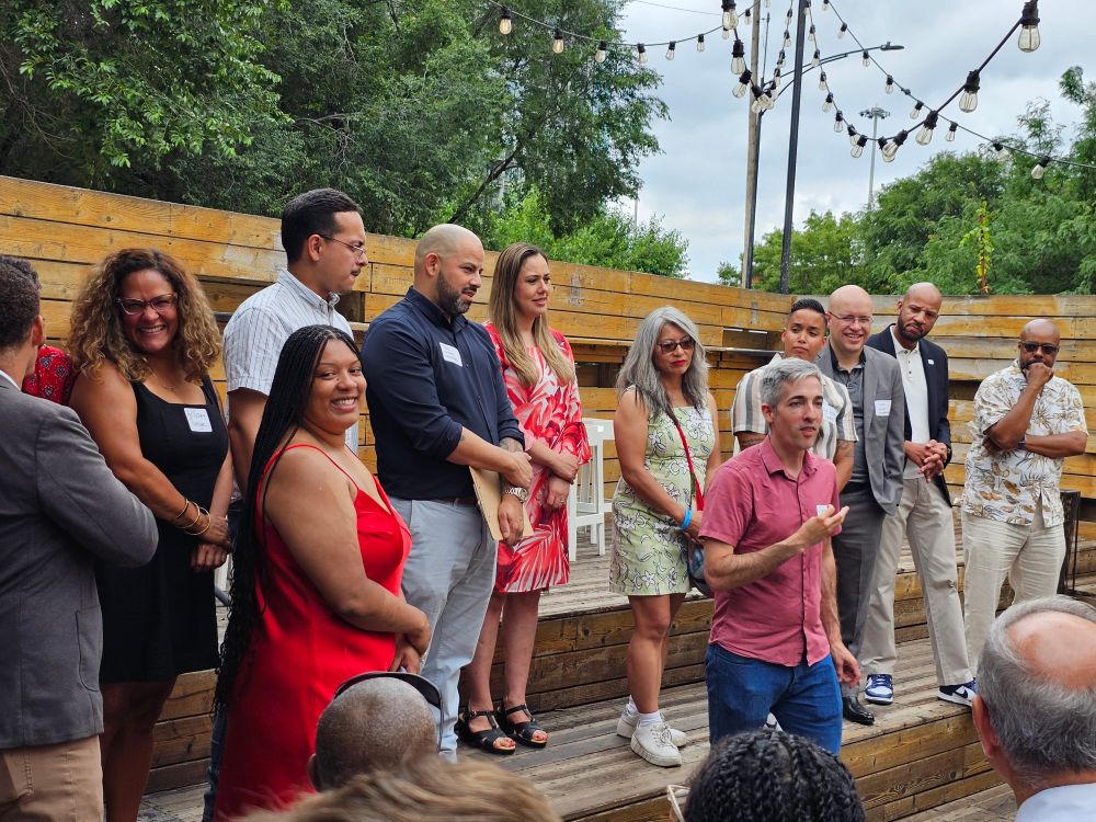 Members of the Progressive Caucus of Chicago City Council, standing on wooden risers outdoors on a patio 