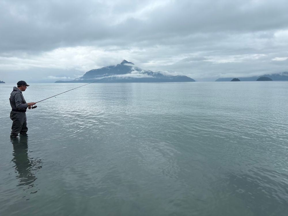 Smooth Howe Sound water with a mountain in the background, a fisherman in the foreground.