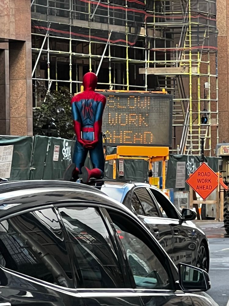 Spider-man stunt double in Glasgow preparing for a shot ahead of a sign saying slow work ahead.