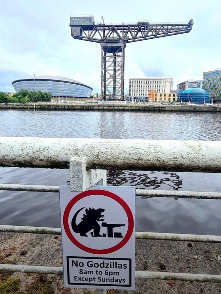 A sign on the riverside opposite Finneston cran, warning No Godzillas 8am to 6pm except Sundays, with a graphic depicting the big kaiju fella menacing the cran and the horrible wee hotel next to it.