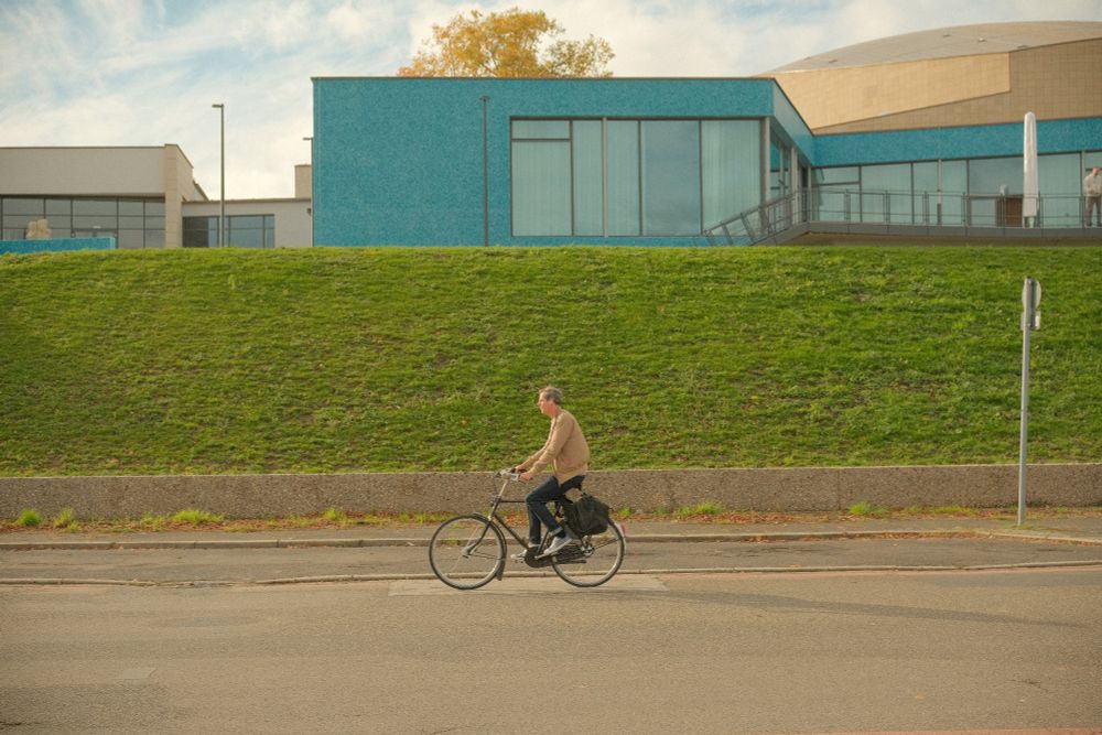 Wes Anderson style photo of a man on a bike in front of a teal building 