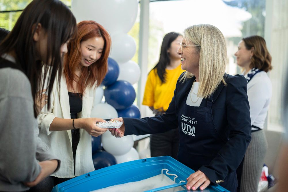 U of T President Melanie Woodin hands an ice cream treat to students at an orientation event, surrounded by others and blue and white balloons.