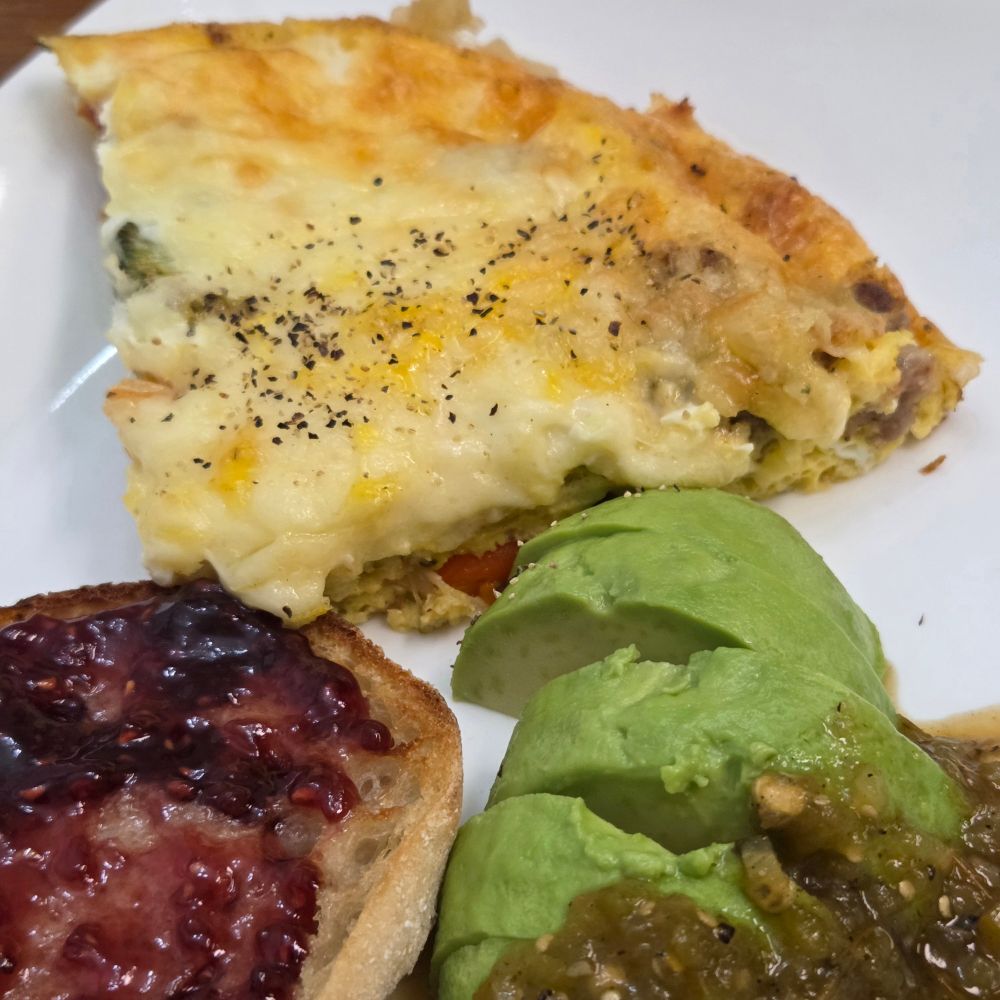 Egg bake of leftover roasted broccoli, sweet potatoes, onion, peppers with bits of sausage. Added whisked eggs, coconut milk, cornstarch, and creole seasoning. Covered in shredded gruyere. Add an avocado half with roasted chili verde and lastly sourdough dark toasted English muffin with red raspberry jam.
