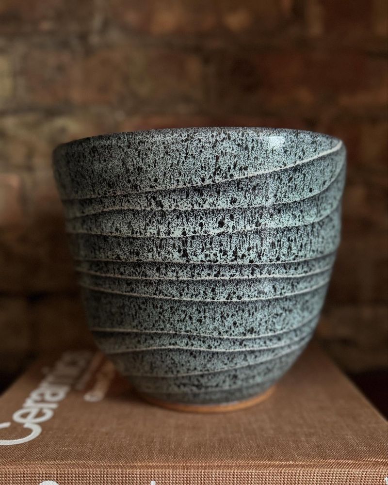 Picture of speckled green vase in front of a brick wall