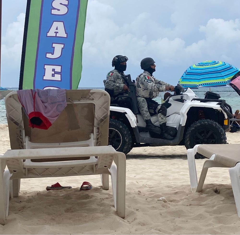 Two cops in camo riding on an ATV across the beach