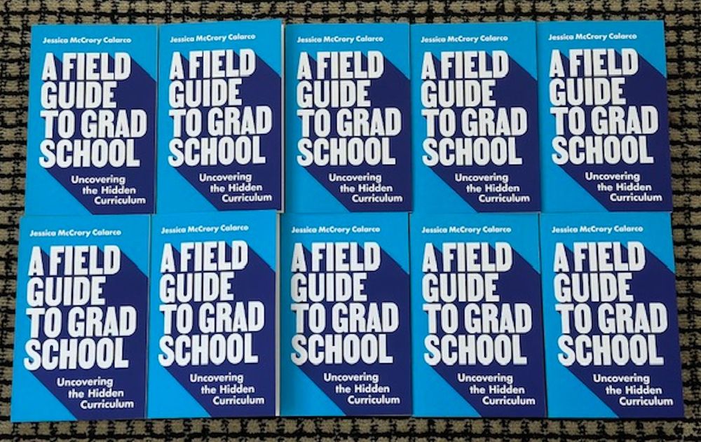 A 2x5 array of copies of "A Field Guide to Grad School" arranged on a floor.