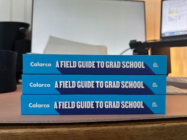 Stack of 3 copies of "A Field Guide to Grad School" written by Dr. Jessica Calarco on a desk. 