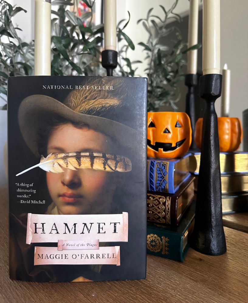 book on table with stacked books, candle holders and pumpkin shaped candle in background 