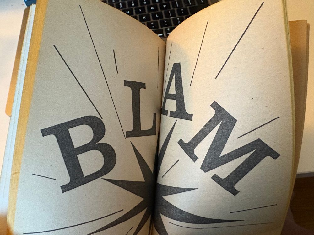 In an old paperback book, a two page spread of "BLAM" with an explosion effect.