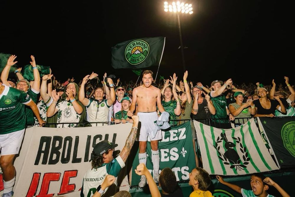 a crowd of Vermonter football fans celebrate a national semi-final win on penalties. most notably, there’s a flag that says “ABOLISH ICE”