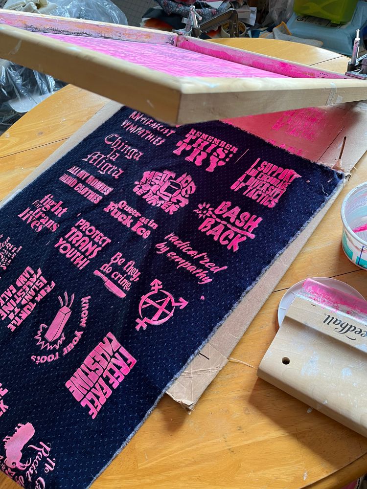 A sheet of fabric with patch designs printed onto it in pink ink, with screen above 