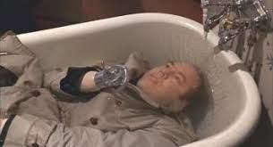 Man in a trench coat with a hook for a hand is drowned in a bath. Eyes open. Taps running