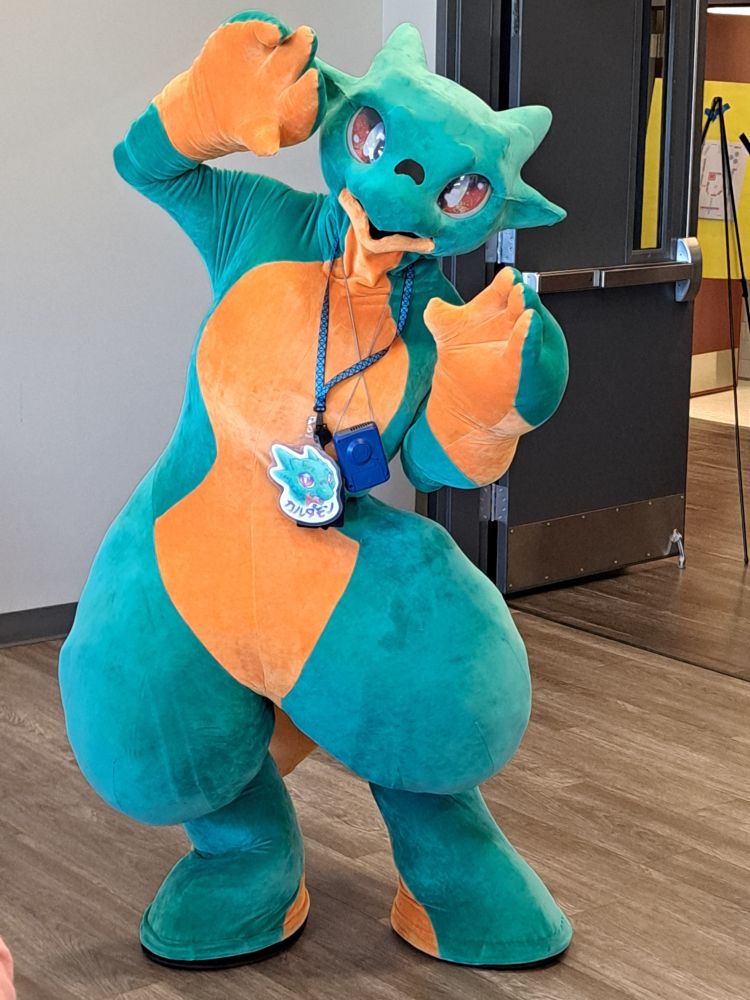 Karudamon, a green dragon fursuit with orange patches on the belly, hands, feet, and tail.